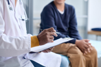 Doctor writing notes while patient sits on exam table